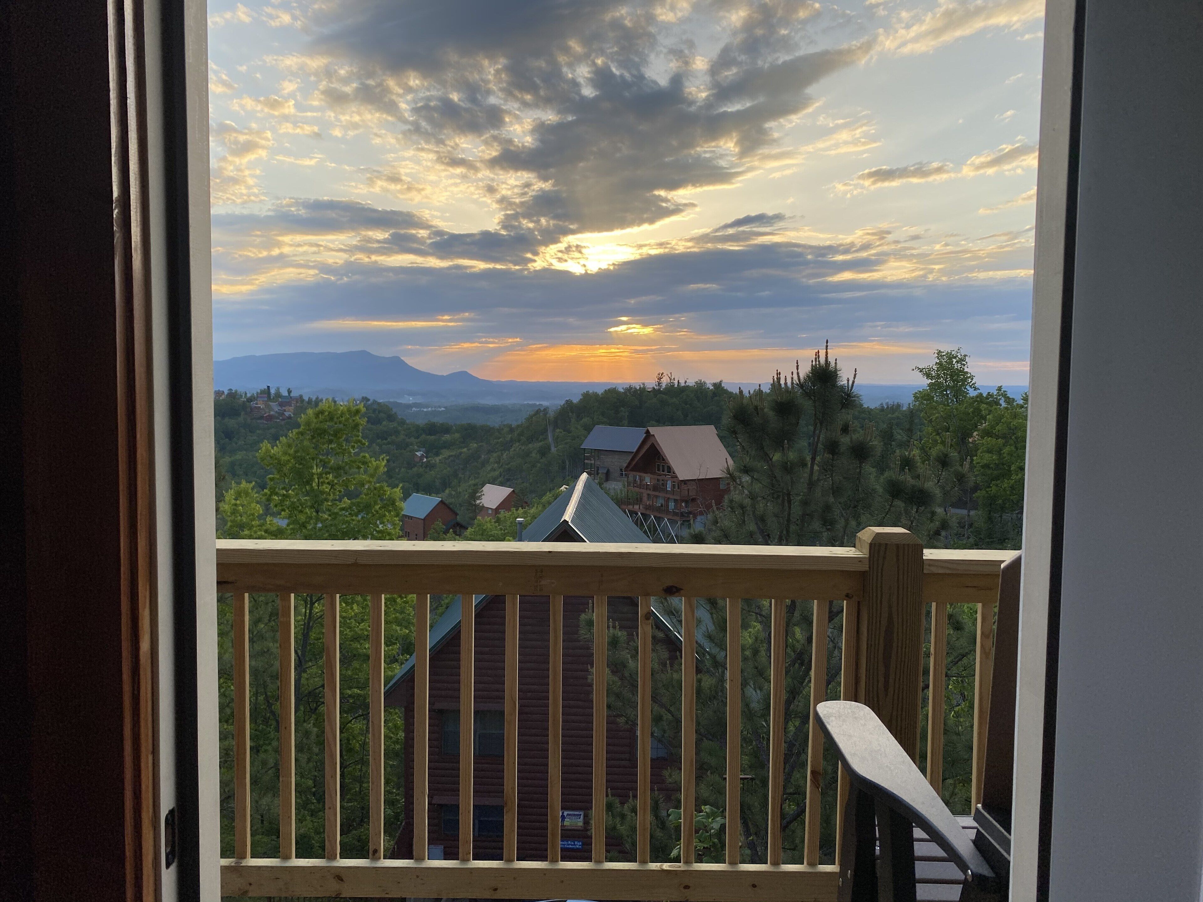 Un balcon en bois offrant une vue sur un paysage montagneux et un coucher de soleil.