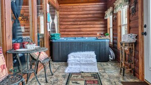 Ein gemütliches Blockhaus-Interieur mit Holzausstattung, einem kleinen runden Tisch mit Stühlen, einem weißen, flauschigen Hocker und einer Whirlwanne.