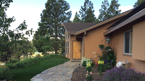 A house with a stone pathway leading to a wooden door, surrounded by a well-maintained garden with various plants and flowers.