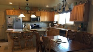 A kitchen with wooden cabinets, a central island with bar stools, a dining table with chairs, and a stove.