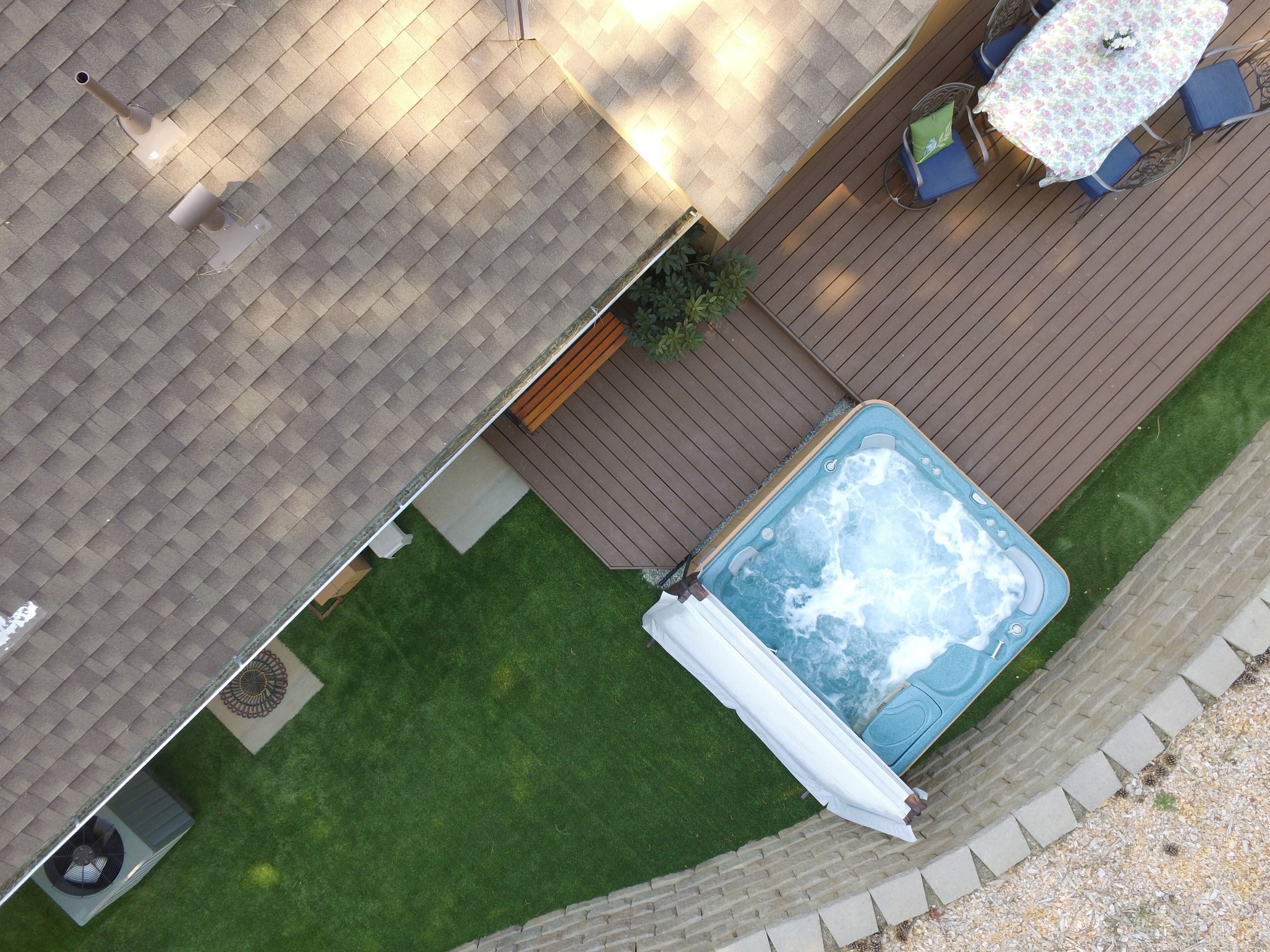 Une terrasse sur le toit avec un jacuzzi, une table et des chaises, et un petit espace aménagé en jardin.
