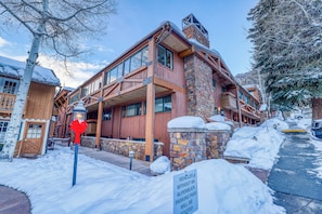 A wooden building with stone accents, a sign indicating no parking without a pass, and snow on the ground. - Upscale & Charming Condo  (Aspen)