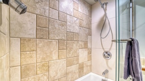 A bathroom with beige tiles, a glass shower enclosure, and a white bathtub. - Upscale & Charming Condo  (Aspen)