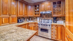 A kitchen with wooden cabinets, granite countertops, a stainless steel stove, and a coffee station. - Upscale & Charming Condo  (Aspen)