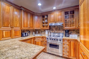 A kitchen with wooden cabinets, granite countertops, a stainless steel stove, and a coffee station. - Charming & upscale Condo in the Heart of Aspen (Aspen)