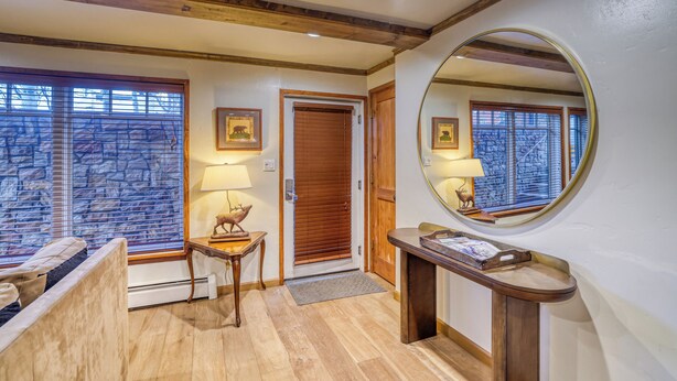 A hotel entrance with a wooden bench, a small table with a lamp, a mirror, and a door with a wooden frame. - Upscale & Charming Condo  (Aspen)