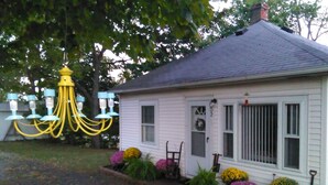 A white house with a gray roof, a front porch, and a yellow chandelier.
