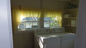 A laundry room with two stacked washers and dryers, a window with yellow curtains, and a laundry basket.
