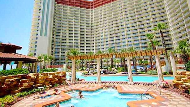 A large hotel with multiple floors, a central swimming pool, and surrounding palm trees. - Welcome to your Gulf Coast Paradise with Stunning Ocean Views & Extras Galore!!! (Panama City Beach)