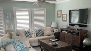 A living room with a beige sofa, a coffee table, a TV, and a ceiling fan.