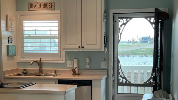 A kitchen with a view of a beach through a glass door, white cabinets, and a sign that reads "BEACHHOUSE".