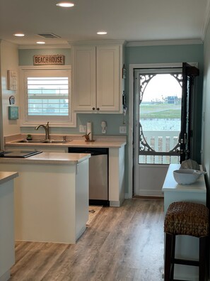 A kitchen with a view of a beach through a glass door, white cabinets, and a sign that reads "BEACHHOUSE". - Intercoastal water view! Pet Friendly! Free WIFI! (Rockport)