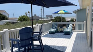 A wooden deck with a blue chair and a large umbrella, a small table, and a view of the ocean.
