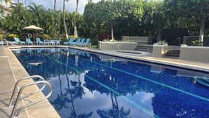 Una piscina con agua azul cristalina, rodeada de sillones de descanso y palmeras.