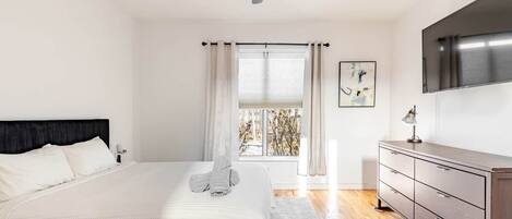A bedroom with a bed, a ceiling fan, a window with curtains, a dresser, and a painting on the wall.
