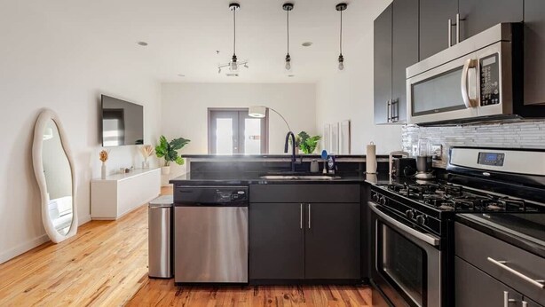 A modern kitchen with stainless steel appliances, a wooden floor, and a minimalist design. - Walk to Stadium + GWCC | Modern 2BR w Parking (Atlanta)