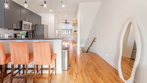 A modern kitchen with dark cabinets, a central island, and three orange chairs. - Walk to Stadium + GWCC | Modern 2BR w Parking (Atlanta)