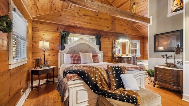 Un dormitorio acogedor con techo de madera, una cama grande con manta de lunares, un aparador y un espejo.