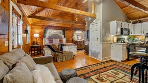 Acogedor interior de cabaña de madera con techo de madera, una cama grande, una zona de comedor y una cocina.