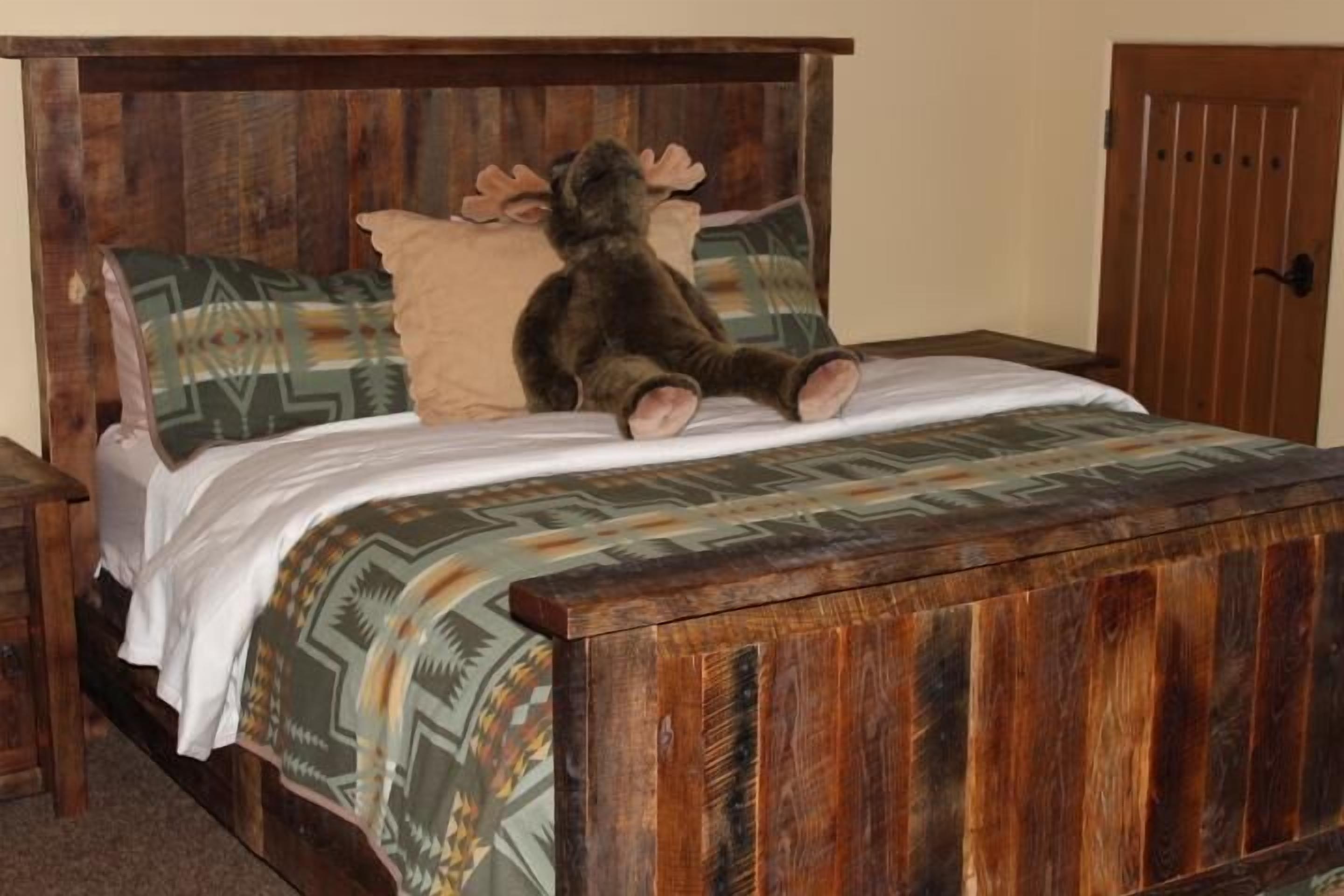 Una cama de madera con un peluche de alce, almohadas estampadas y un cabecero a juego.