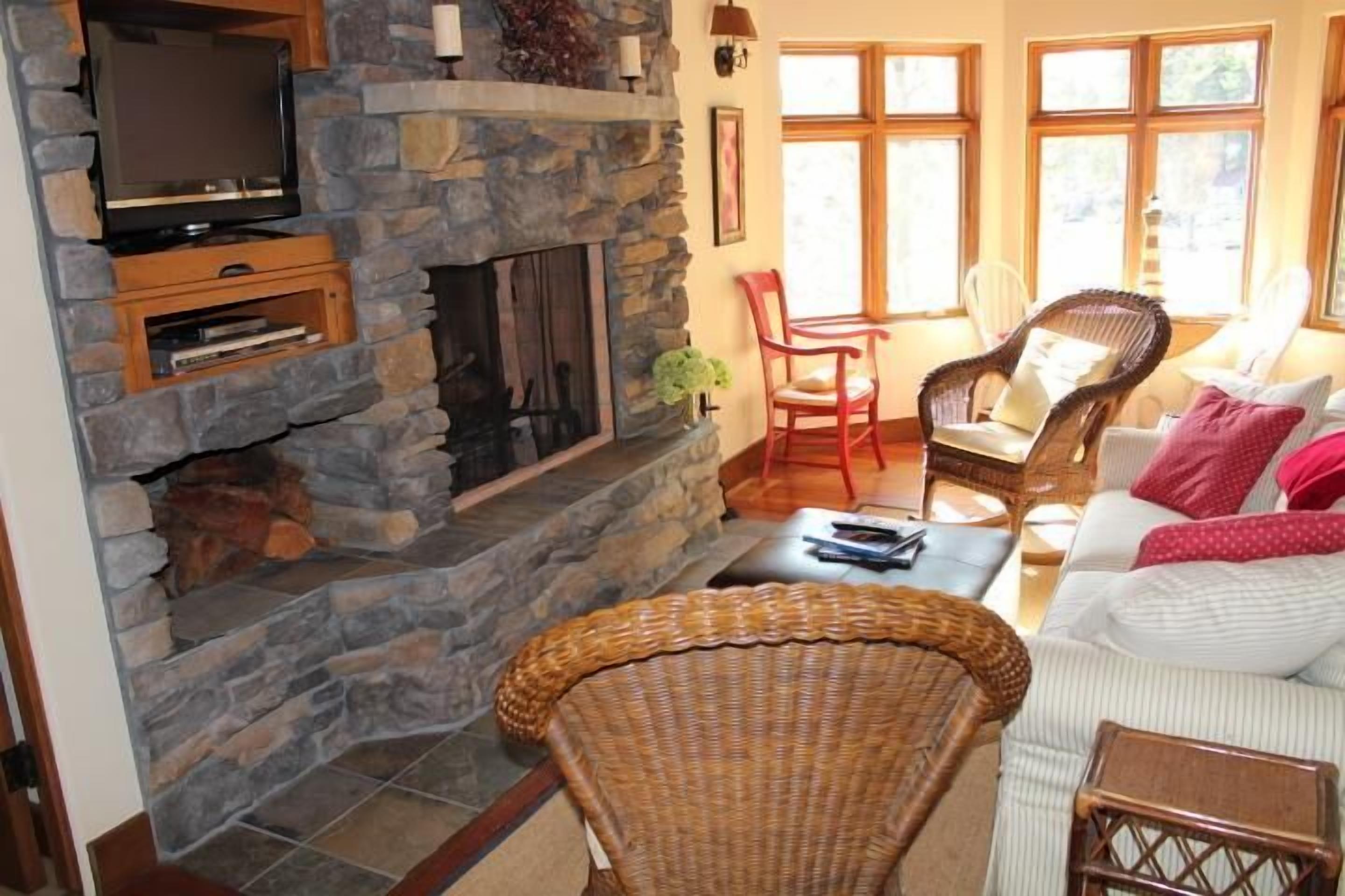 A cozy living room with a stone fireplace, comfortable seating, and a television.