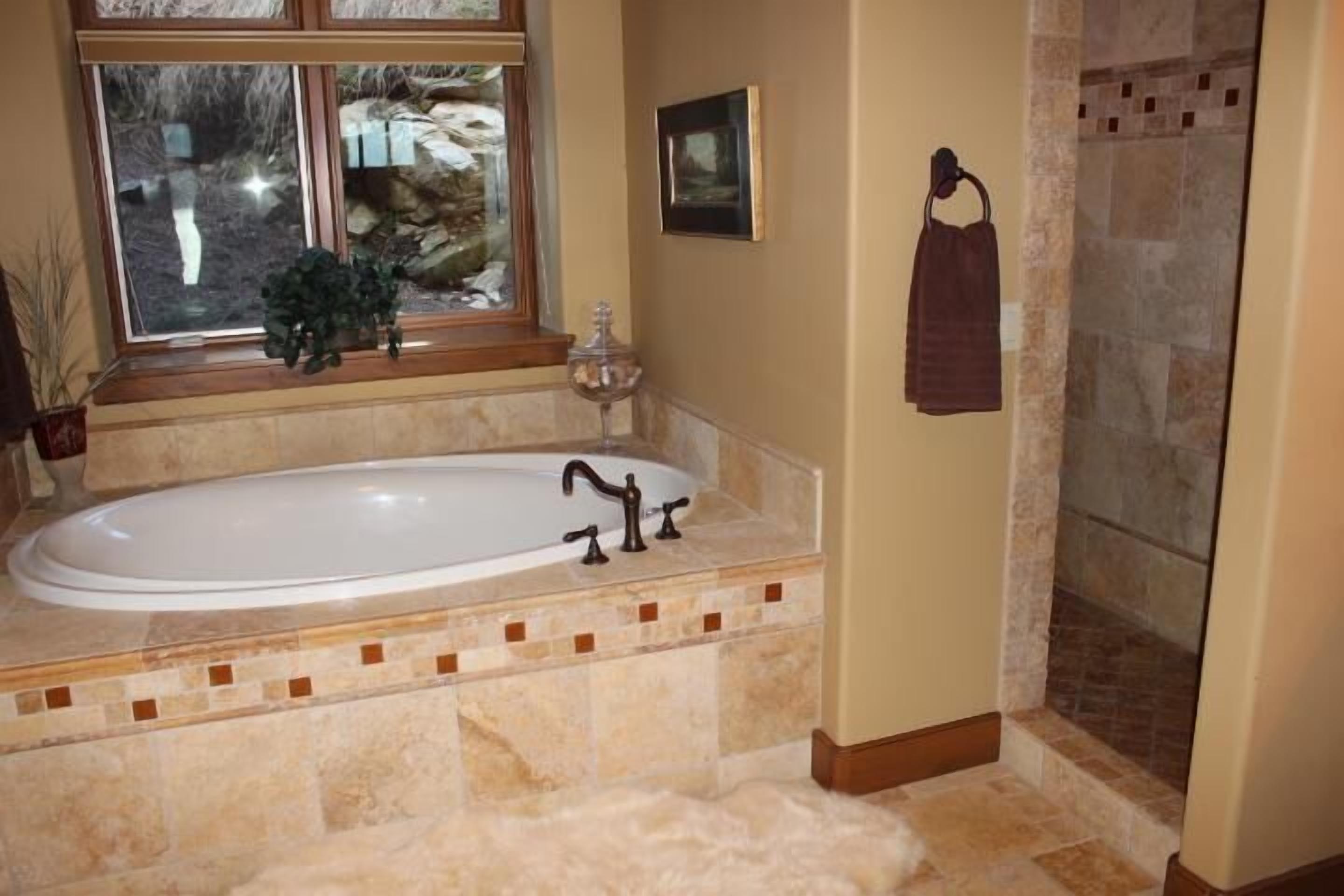A bathroom with a large bathtub, a window with a view of rocks, a towel rack, and a shower area.