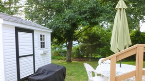 A small white house with a covered table and chairs, a covered object, and a green umbrella.