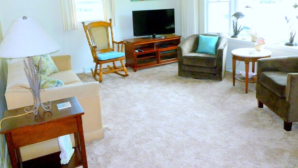 A living room with a television, a rocking chair, a sofa, and a small table with a lamp.