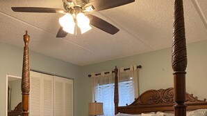 Ein Himmelbett mit Deckenventilator, Nachttischlampe und einem fenster mit Vorhängen.