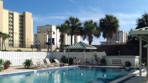 Ein rechteckiger Swimmingpool mit einer Fliesenbordsteinkante, umgeben von Liegestühlen und einer überdachten Sitzgruppe.
