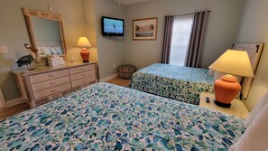 A hotel room with two beds, a television, a mirror, a lamp, and a framed picture on the wall.