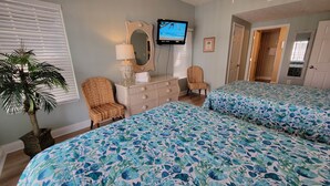 Habitación de hotel con dos camas, televisión, cómoda, silla y planta en maceta.