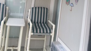 A room with a window, a door, a striped chair, a small table, and wall decorations including a sign and various items.