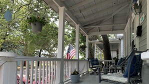 A covered porch with white railings, potted plants, and outdoor furniture.