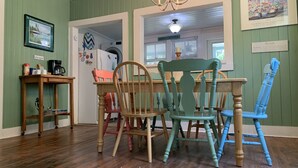 A dining area with a wooden table and chairs, a chandelier, and a refrigerator with magnets.