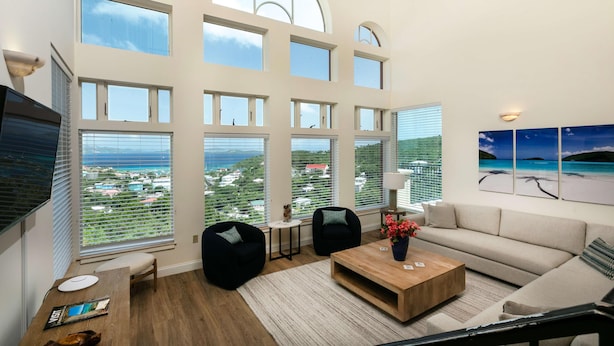 A spacious living room with large windows, a flat-screen TV, a wooden coffee table, and a sofa. - Gardenia Newly Renovated with Tesla Power Walls! (St. John)