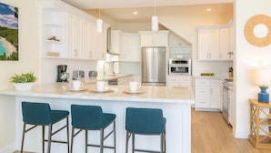 A modern kitchen with white cabinets, stainless steel appliances, and a central island with bar stools. - Gardenia Newly Renovated with Tesla Power Walls! (St. John)