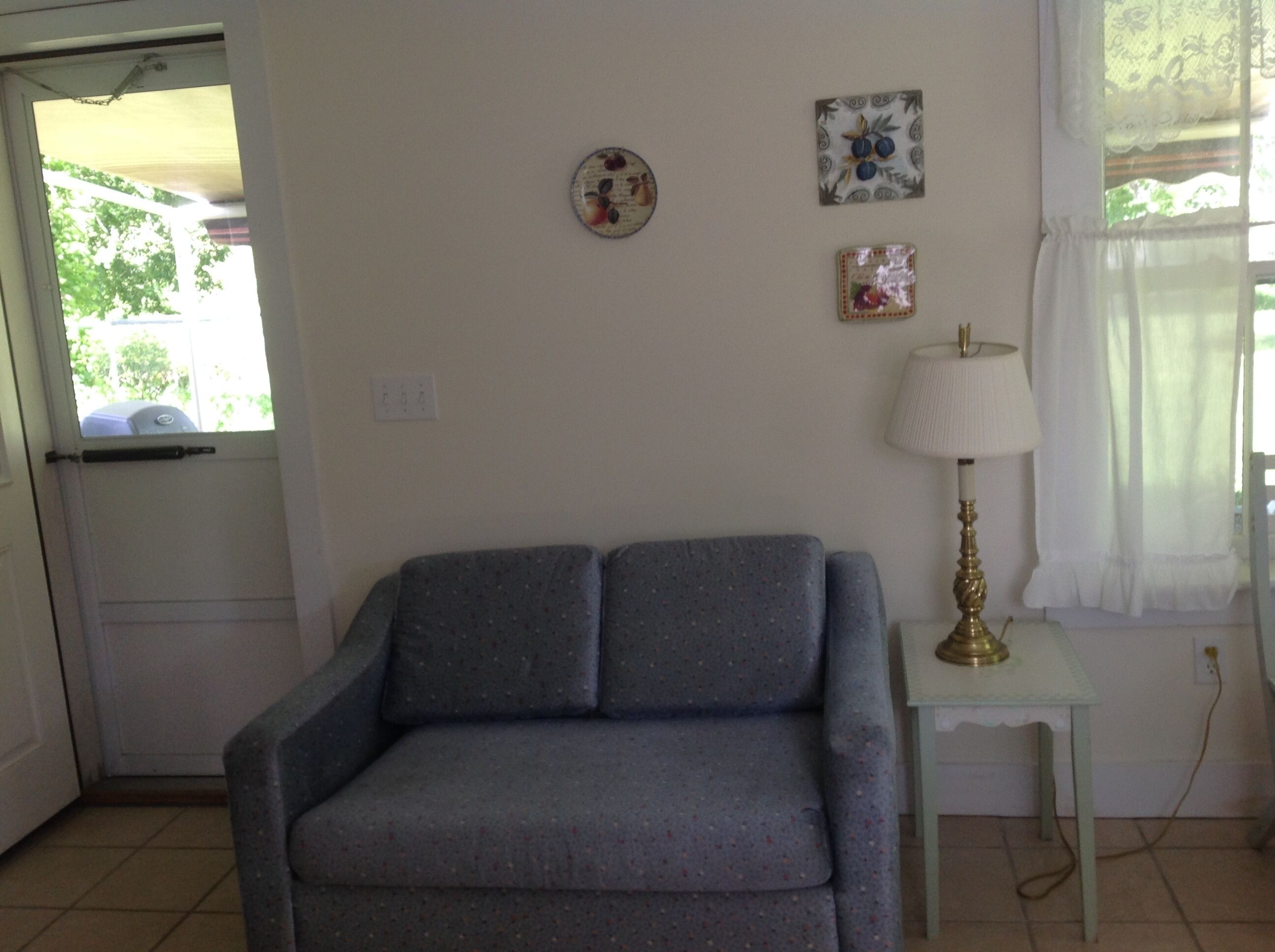 Una habitación con un sofá gris, una mesita blanca con una lámpara y dos adornos en la pared.