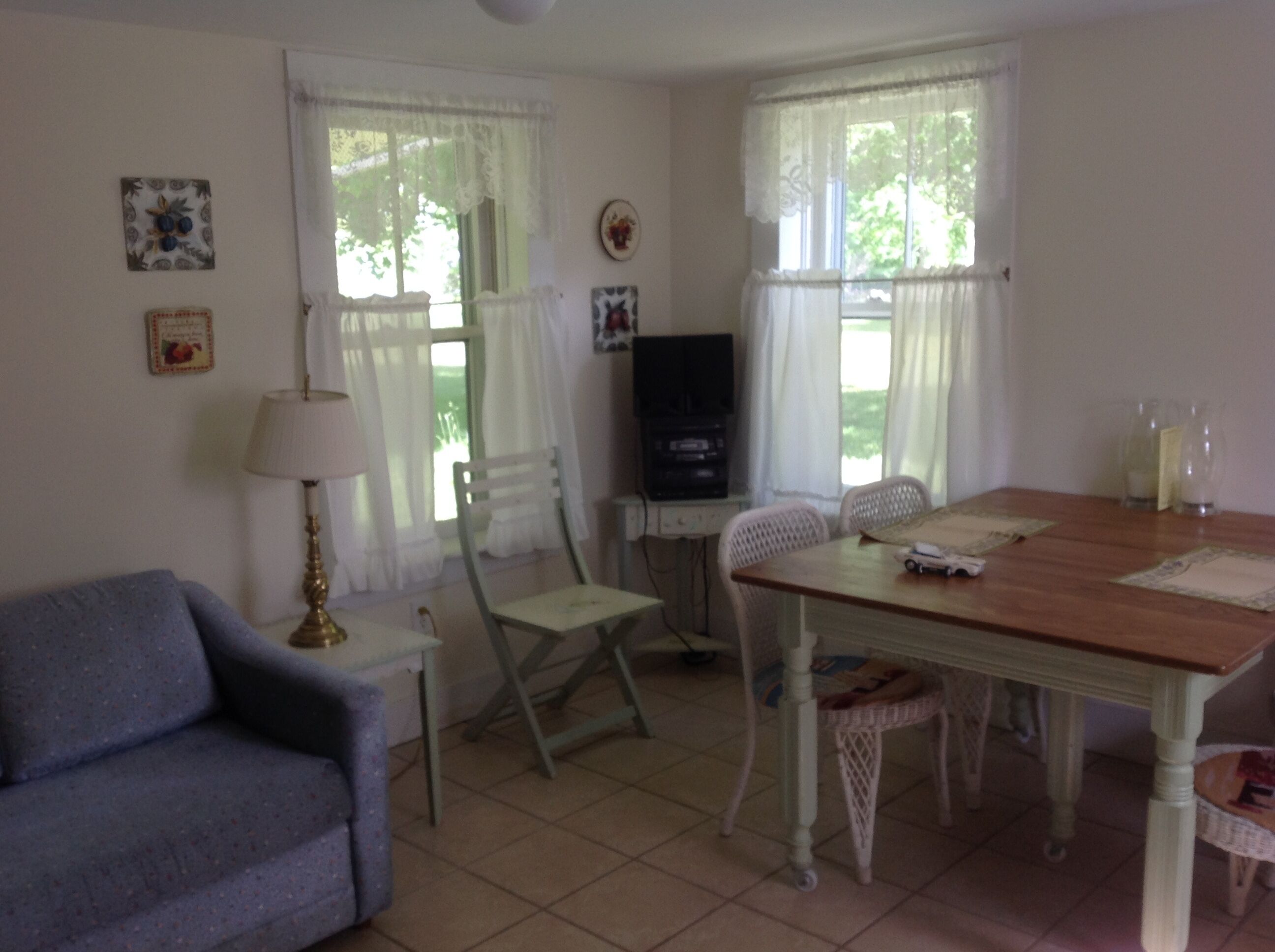 A room with a wooden dining table, two white chairs, a blue sofa, a television, and a lamp.