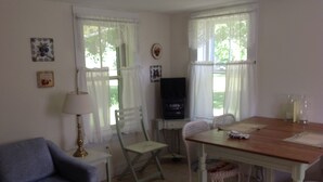Una habitación con una mesa de comedor de madera, dos sillas blancas, un sofá azul, un televisor y una lámpara.