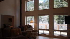 A spacious living room with large windows, a sofa, a chair, and a table. - Beautiful Mountain Retreat Just Minutes From the Slopes!! (Taos Ski Valley)