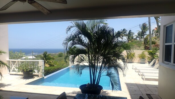 A pool area with a view of the ocean, a ceiling fan, and a table with chairs. - Spacious Indoor/Outdoor living. Private pool. Amazing ocean views (Half Moon Bay)