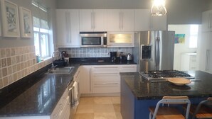 A modern kitchen with white cabinets, a black countertop, stainless steel appliances, and a blue island with bar stools. - Spacious Indoor/Outdoor living. Private pool. Amazing ocean views (Half Moon Bay)