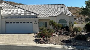 A single-story house with a tiled roof, a garage, and a landscaped front yard with rocks and plants.