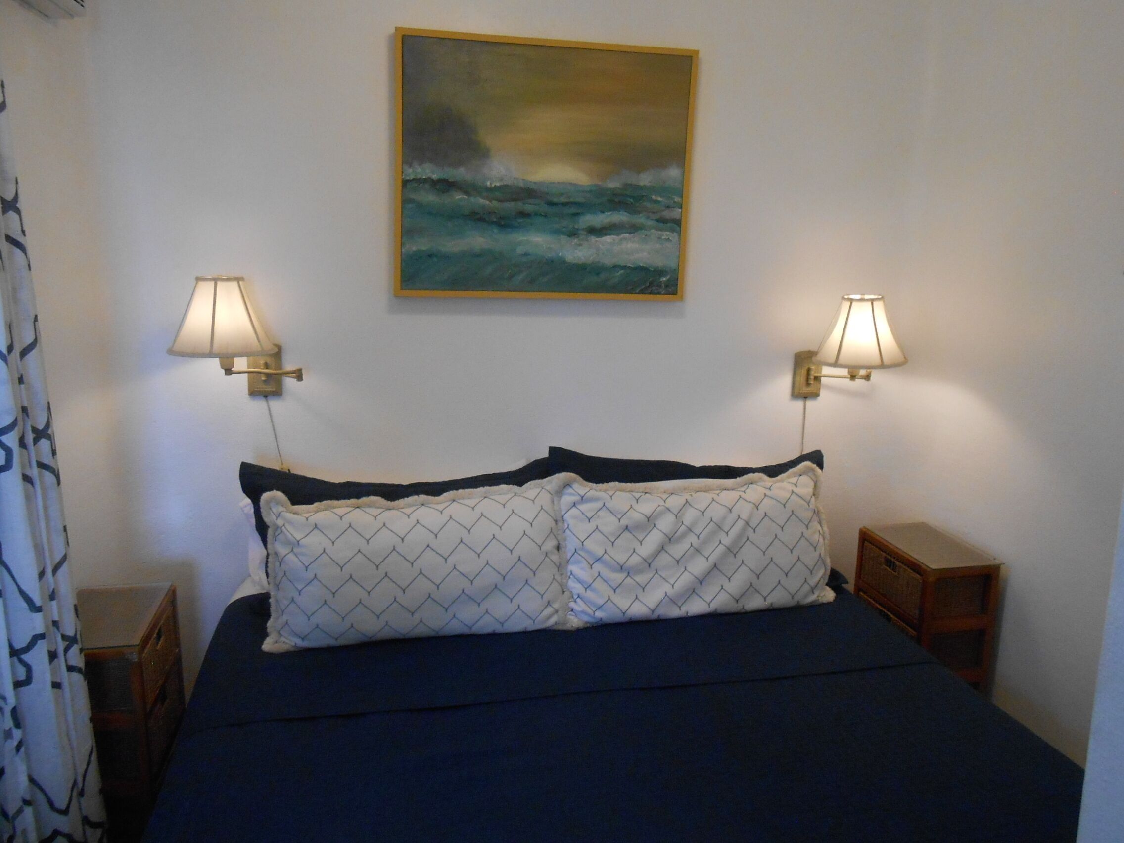 Un dormitorio con una cama, dos lámparas de noche, un cuadro de un mar tormentoso y una cortina.