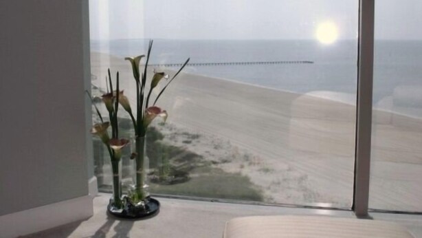 Ein Zimmer mit großem Fenster und Blick auf Strand und Steg.
