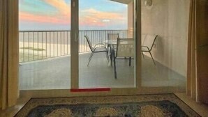 Ein Zimmer mit einer Schiebetür, die auf einen Balkon mit Blick auf den Strand und Sonnenuntergang führt.