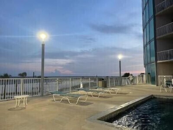 Zona junto a la piscina con sillones de descanso y una pequeña alberca, rodeada por una baranda y un edificio con balcones.