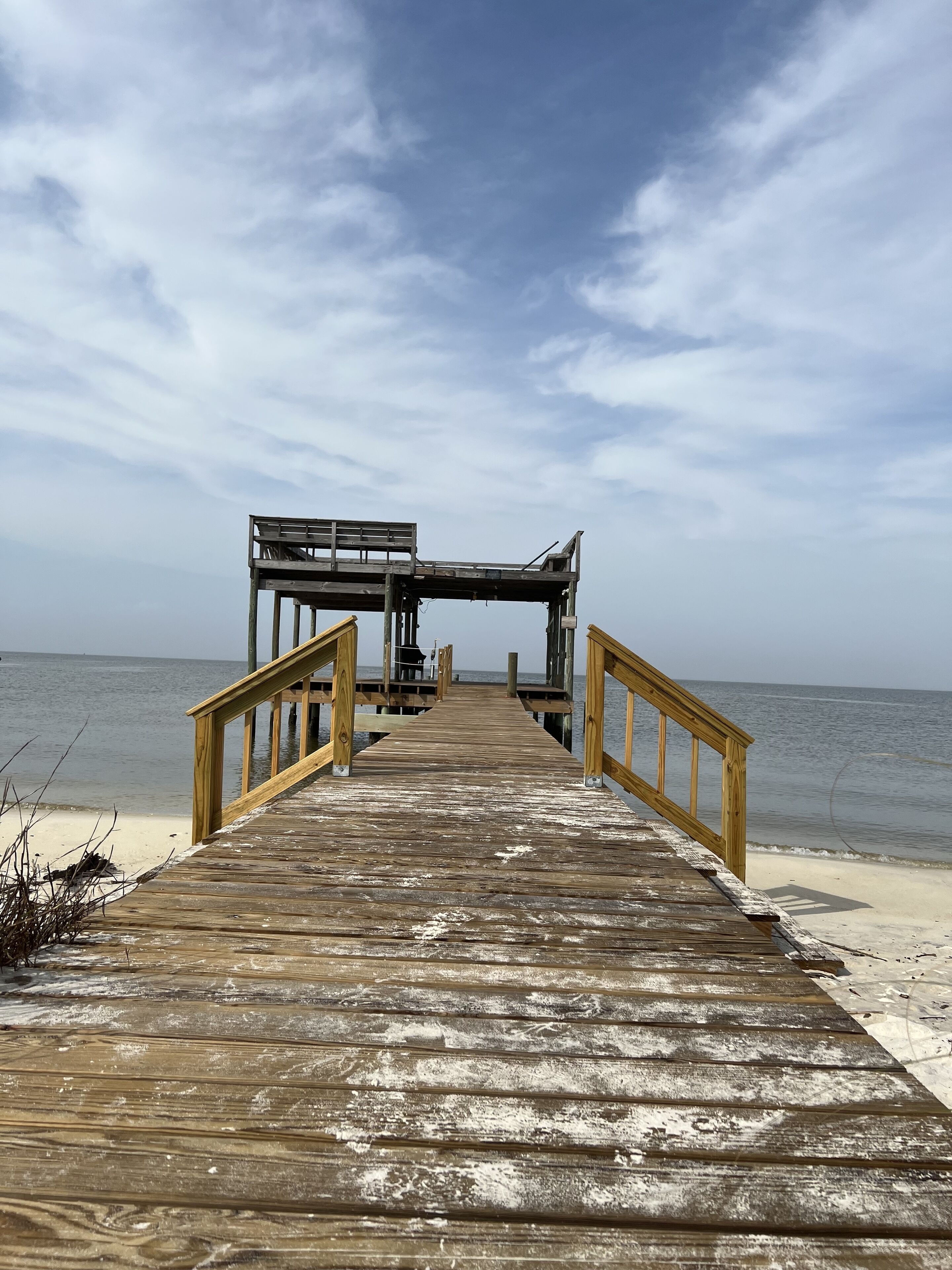 Une jetée en bois mène à une structure dotée d’une rambarde, qui s’étend au-dessus d’une plage de sable.