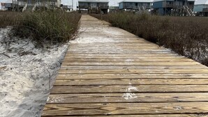 Een houten looppad dat naar strandhuisjes met verhoogde constructies leidt.
